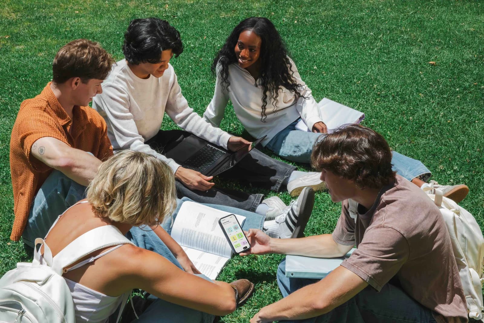 Students studying together outdoors with laptops and course materials.